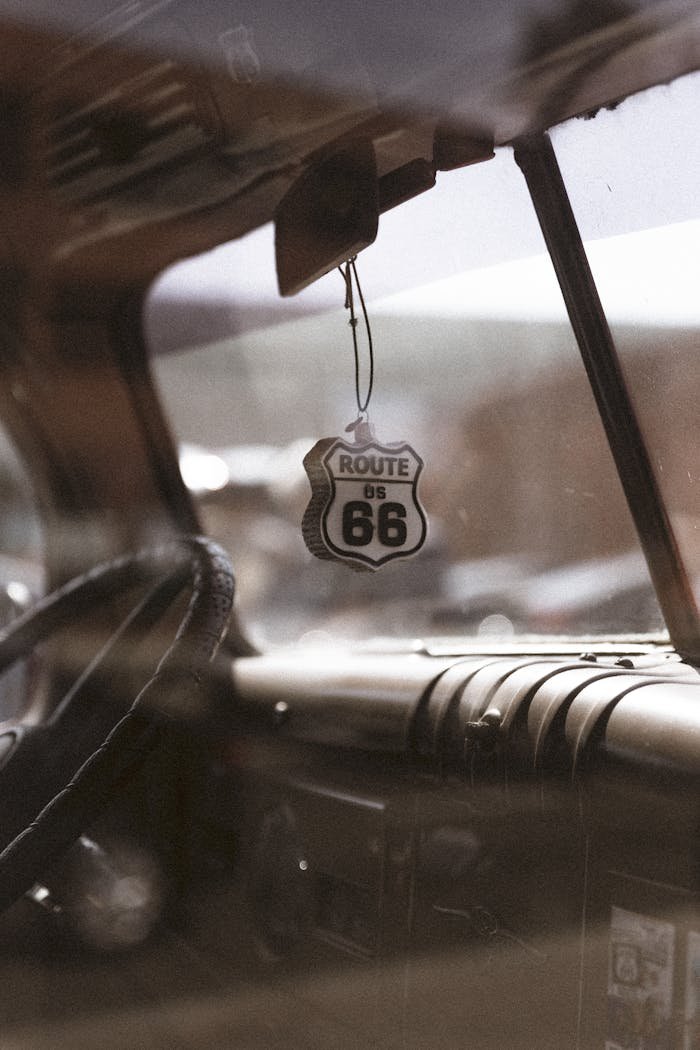 Close-up of a vintage car interior featuring a Route 66 air freshener hanging from the rearview mirror.